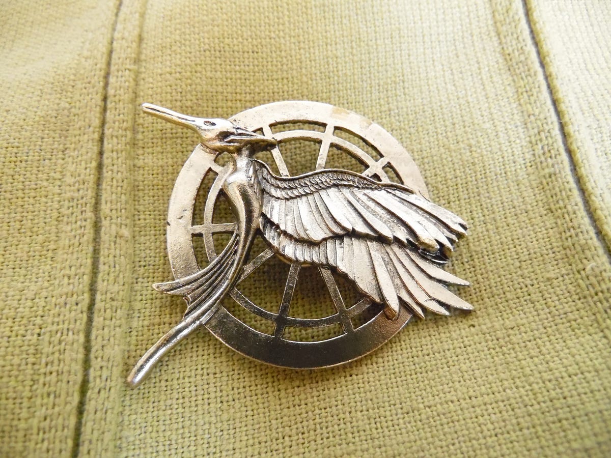 A pin decorated with a mockingjay, a bird commonly depicted in the Hunger Games series.